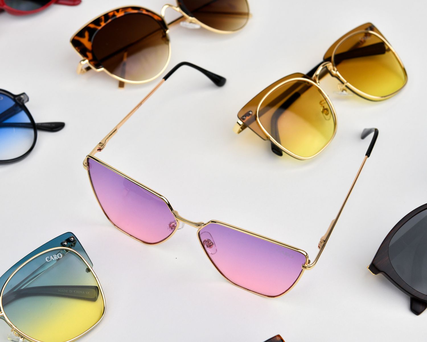 Fashionable sunglasses with gradient lenses in pink, yellow and blue tones arranged on white surface.