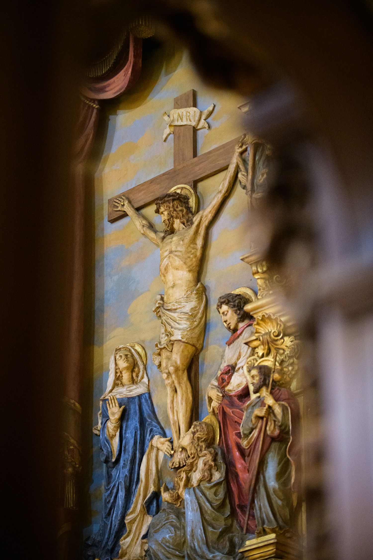 Religious sculpture depicting the Crucifixion scene with figures at the base of the cross in dramatic lighting and colors.