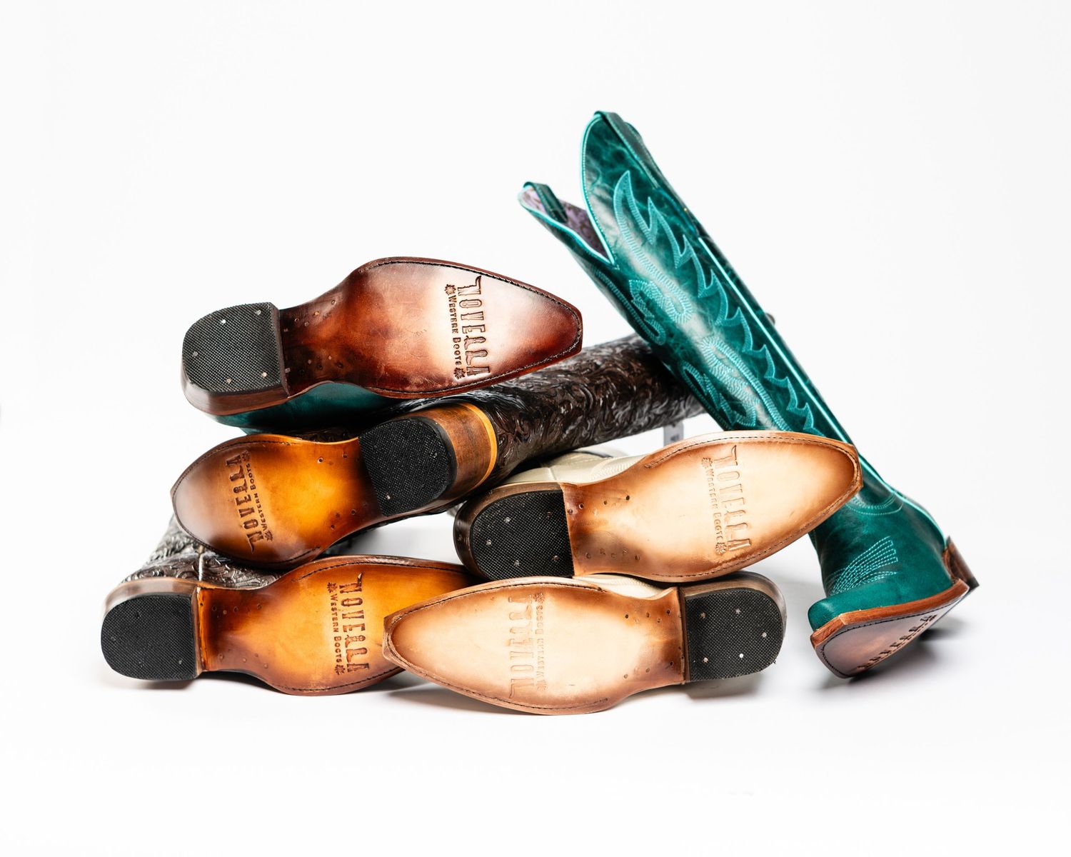 Stack of vintage leather cowboy boots with turquoise boot standing upright.