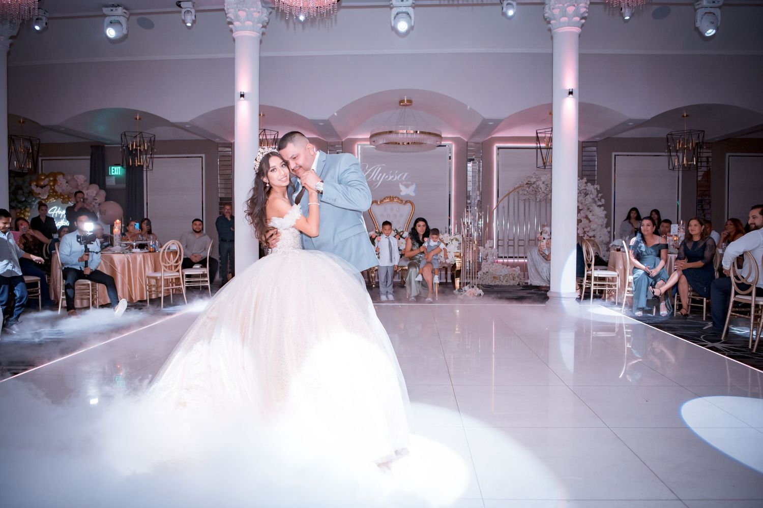 A romantic first dance at an elegant wedding reception with ethereal fog effects on a white dance floor.