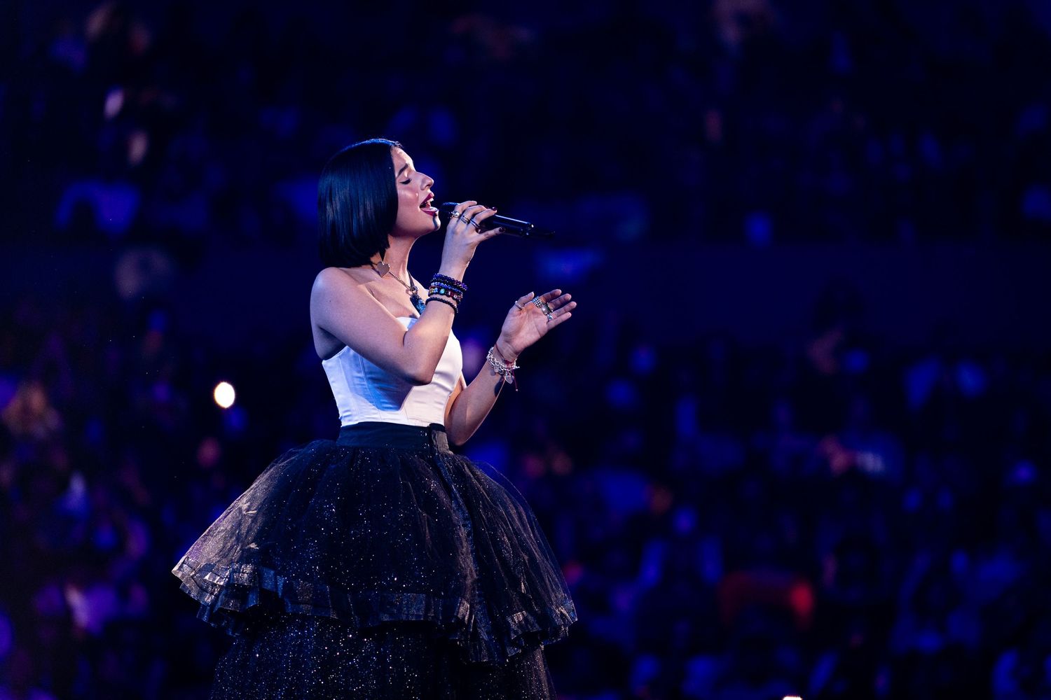 Singer performing on stage in white and black dress under dramatic blue lighting.