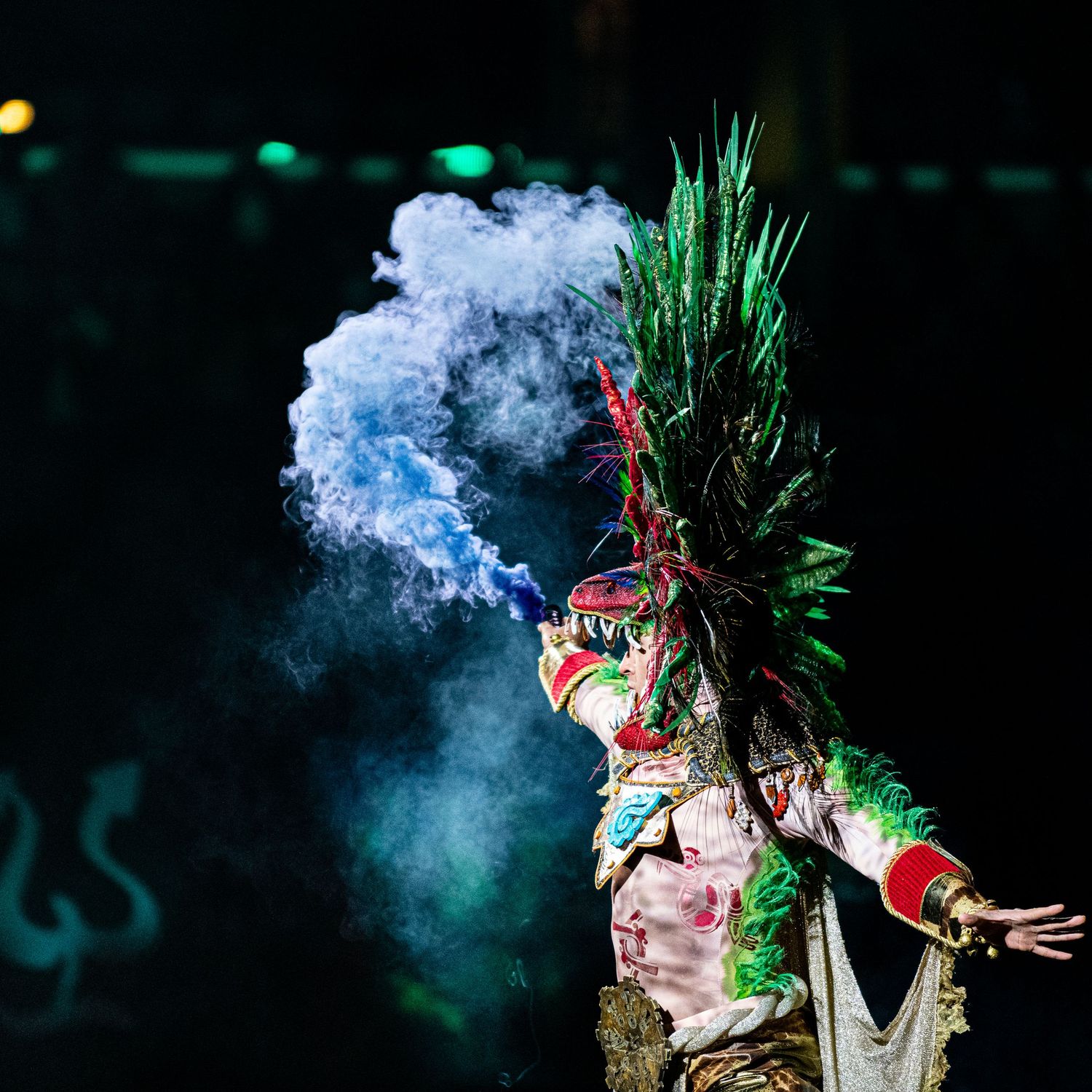 Traditional dancer in ceremonial headdress performing with dramatic blue smoke effects.
