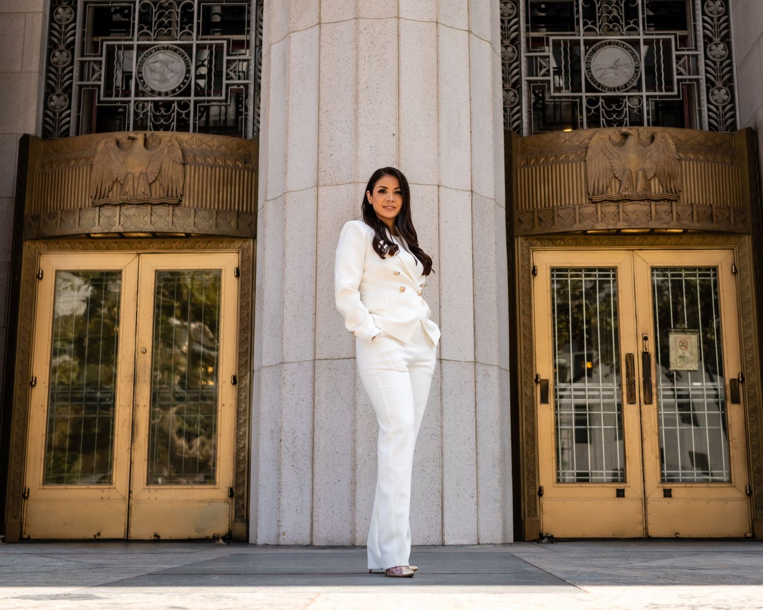 Professional portrait of woman in white suit standing between classic architectural columns.