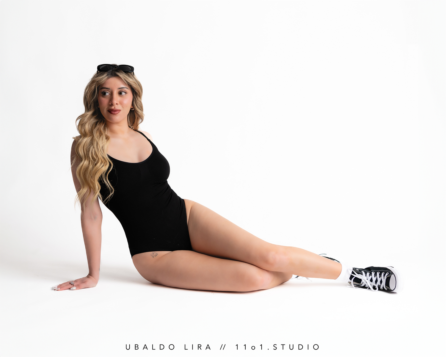 Studio portrait in black bodysuit and sneakers against white background.