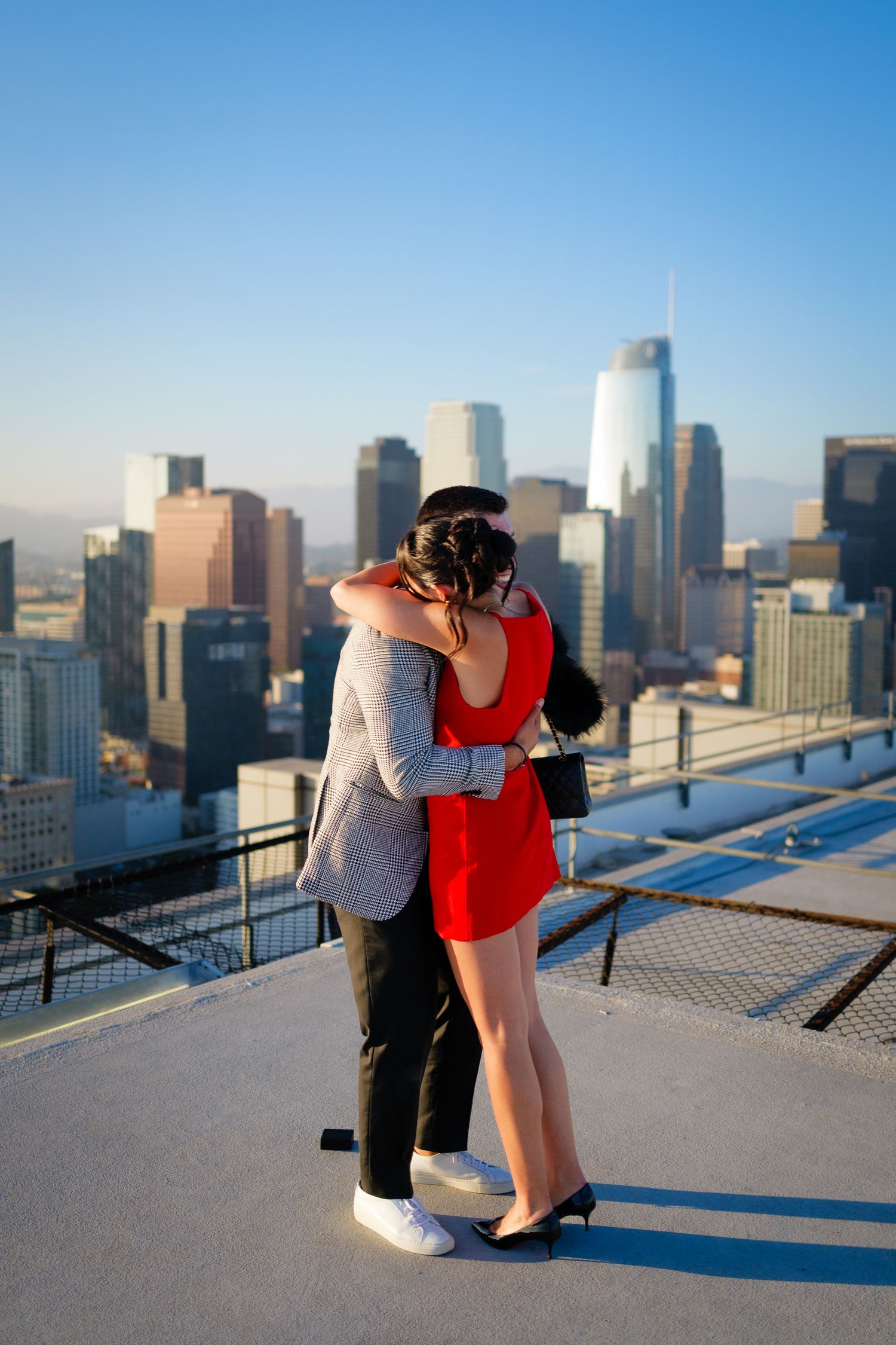 A couple embraces on a rooftop observation deck with the Minneapolis skyline visible in the background on a clear day.