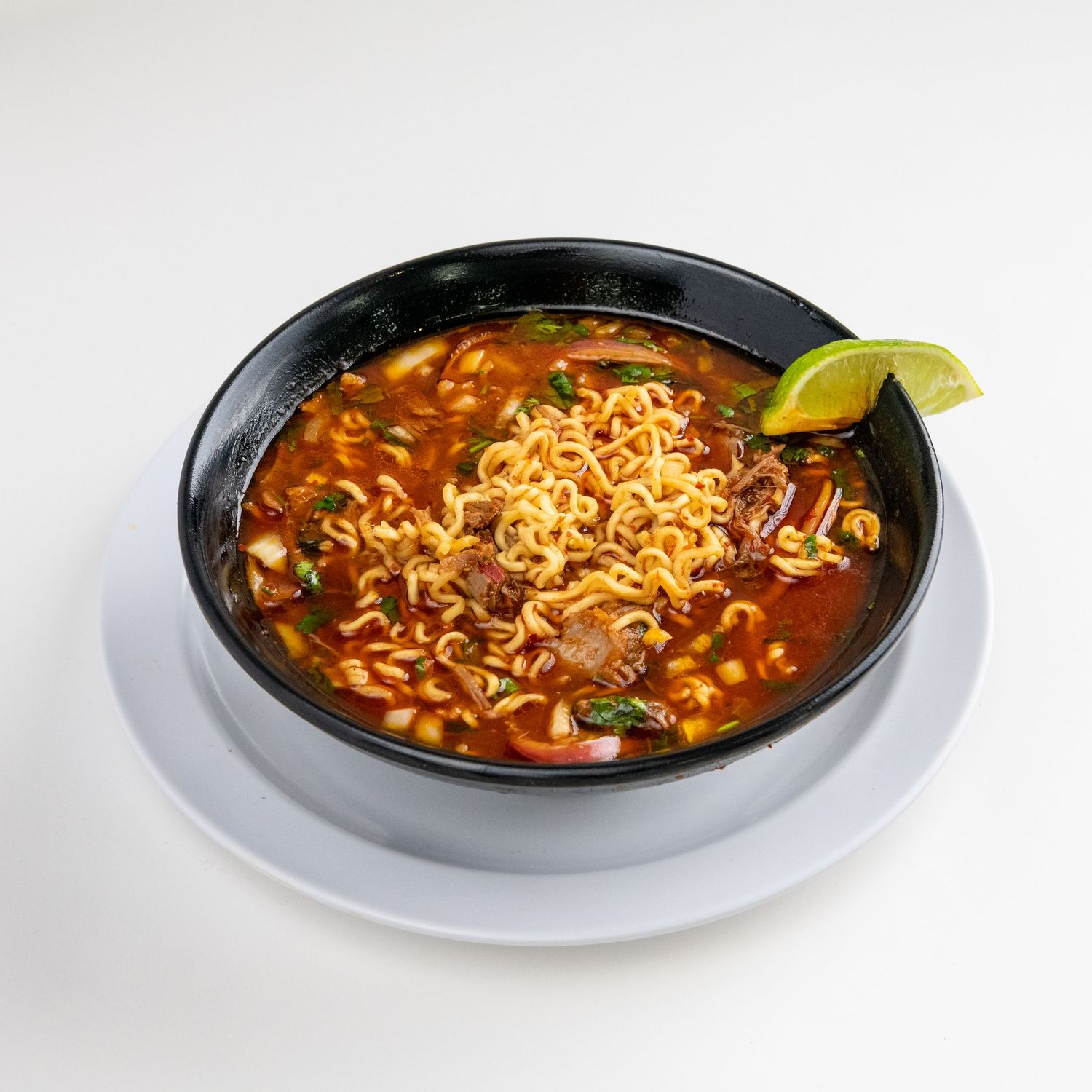 Spicy soup with noodles, vegetables and lime garnish served in black bowl.