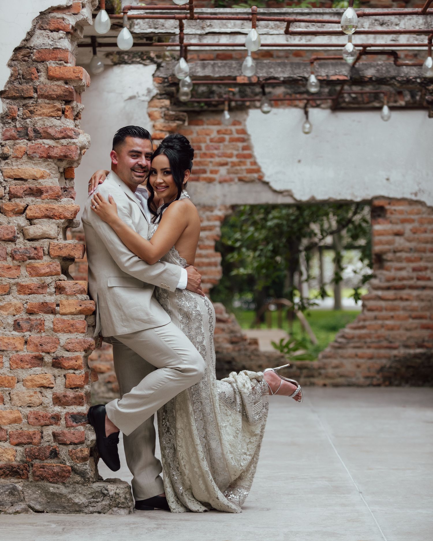 A couple shares a romantic pose against a rustic brick wall archway during their wedding celebration.