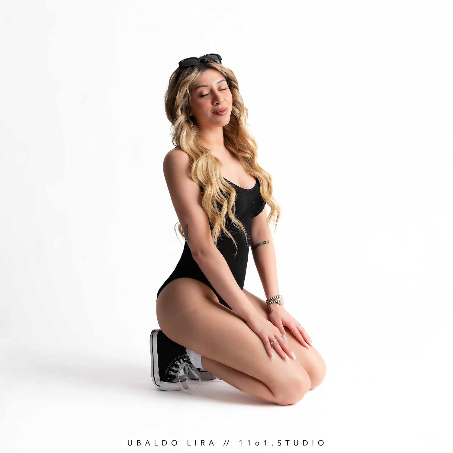 Studio portrait of a model in black bodysuit and sneakers posing on white background.