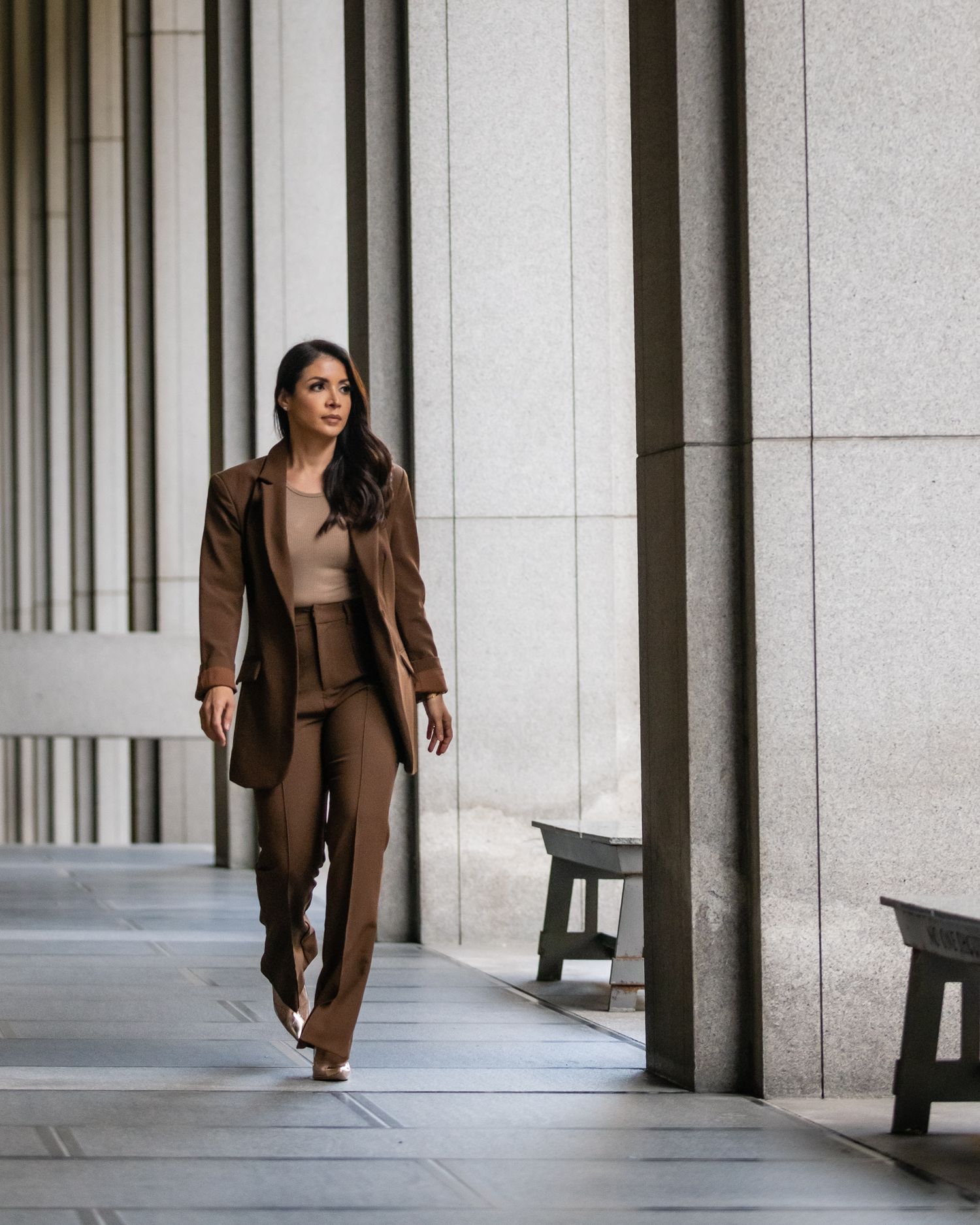 Woman in brown business suit walking confidently through modern architectural colonnade.