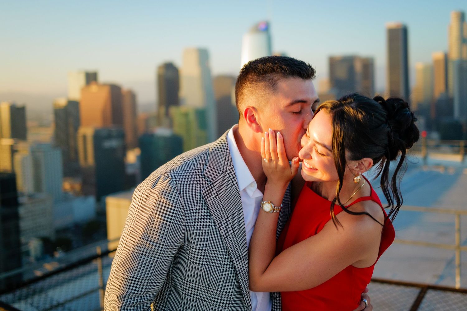 A couple shares an intimate moment on a rooftop with a golden-hour city skyline backdrop.