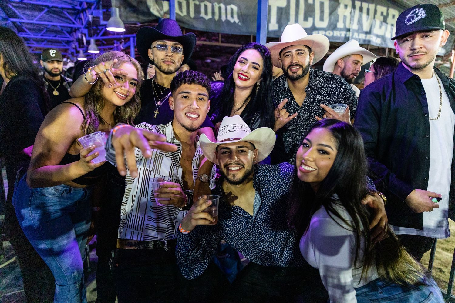 A group of friends in western attire pose together at a nightclub or bar event.