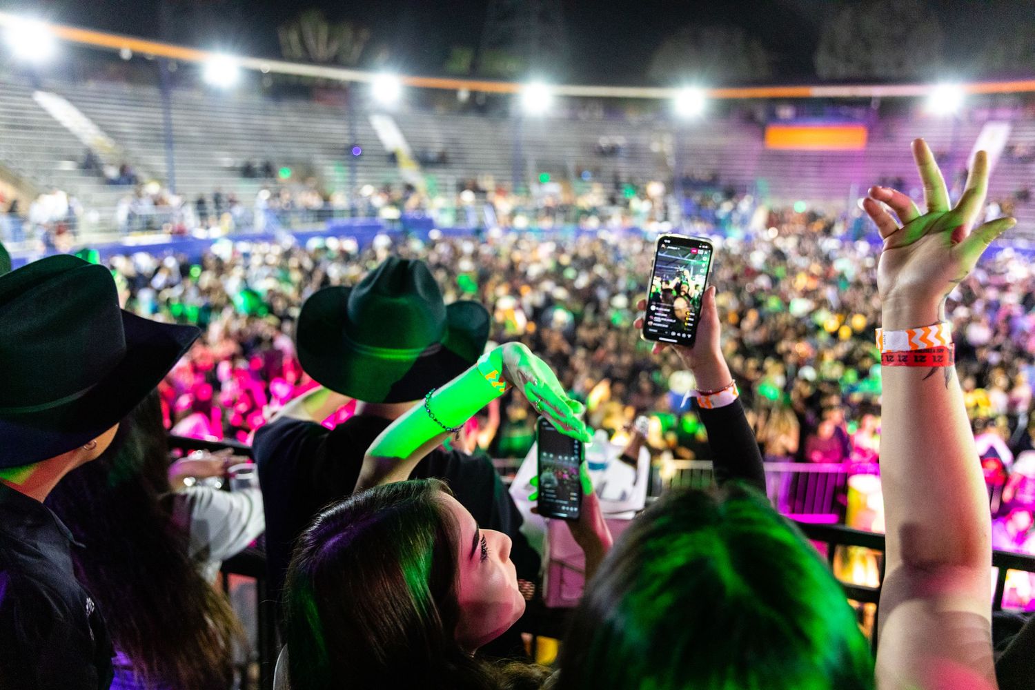 Concert crowd holding up phones to capture performance with colorful stage lighting.