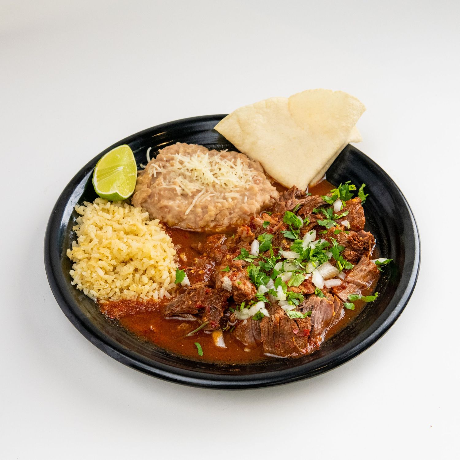 Mexican plate with rice, beans, meat and tortilla garnished with lime and fresh herbs.
