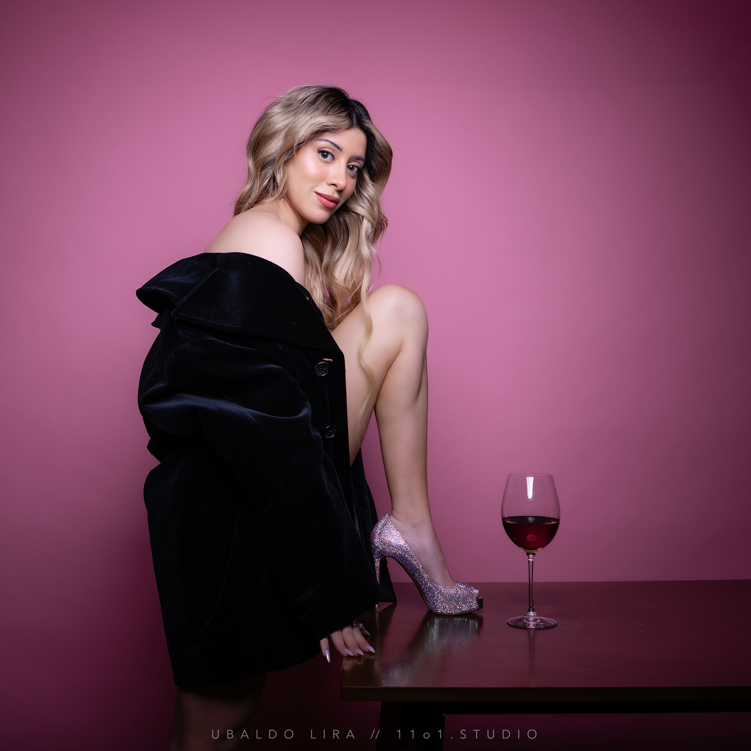 Glamour portrait with black fur coat and wine glass against pink background.
