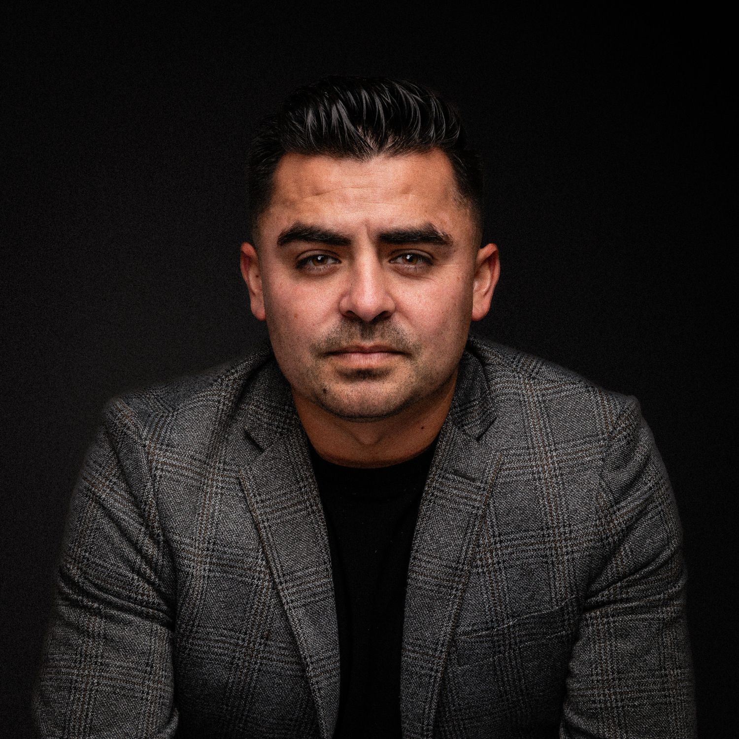 Professional headshot of man in blazer against dark background.