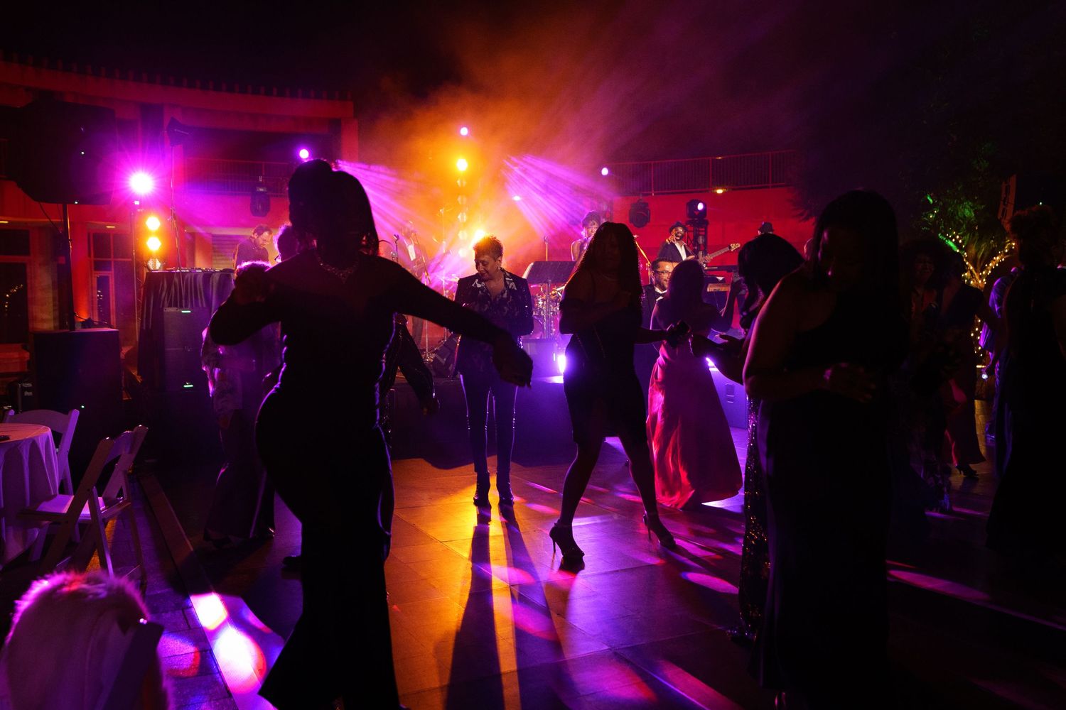 Silhouettes of people dancing at a party with colorful purple and orange lighting.