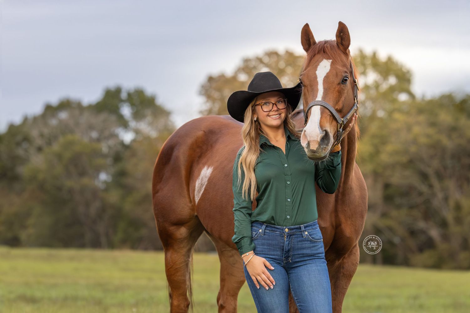A chestnut horse stands in a grassy field with someone wearing a black hat and green shirt on an autumn day.
