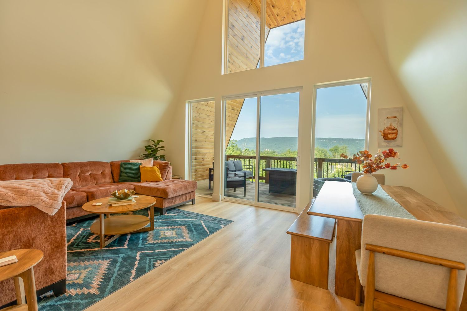 Modern living room with vaulted ceiling, large windows, blue area rug and tan leather sofa overlooking scenic mountain views.