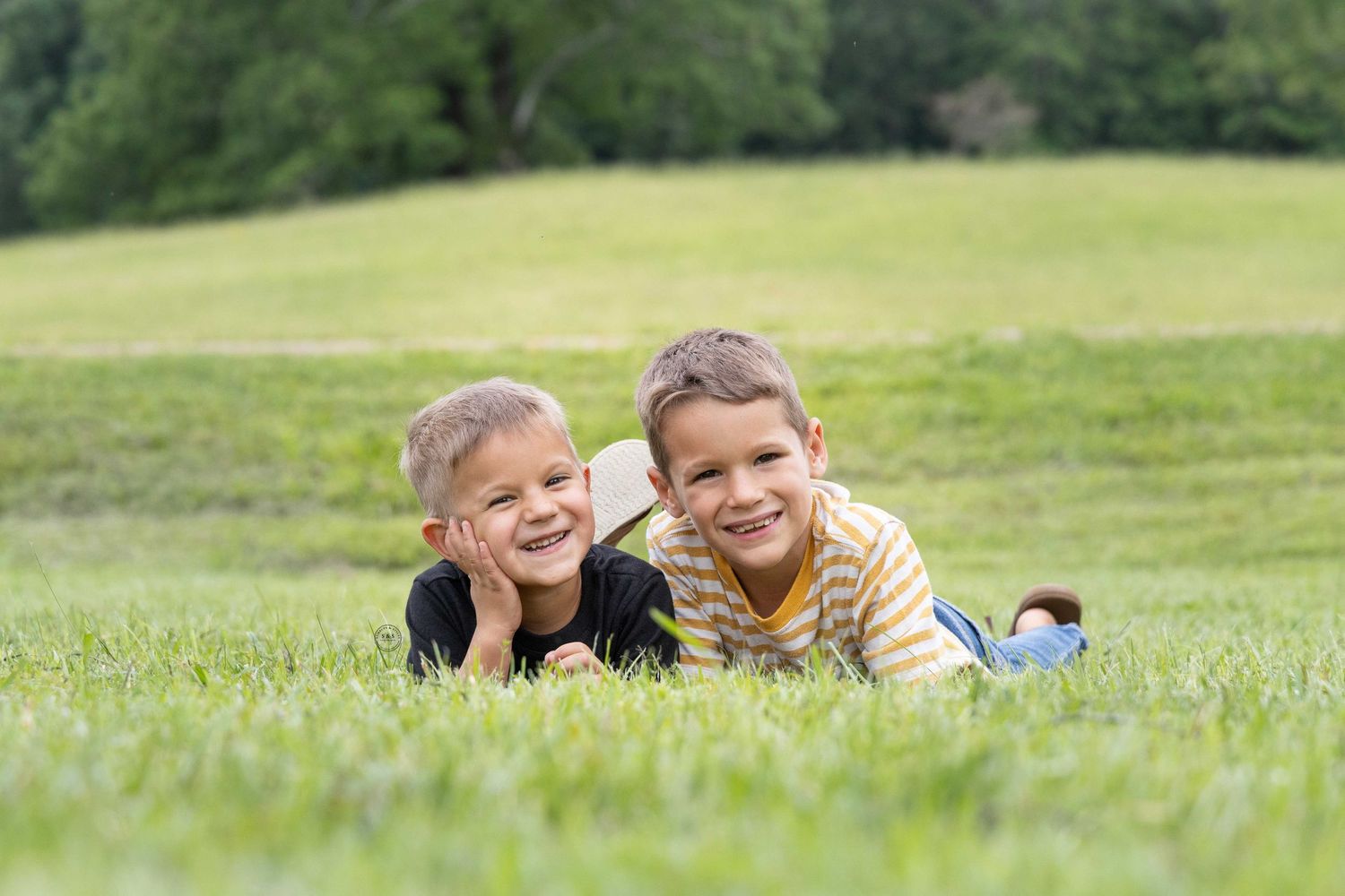 Children play together and laugh while laying on green grass in a sunny meadow on a summer day.