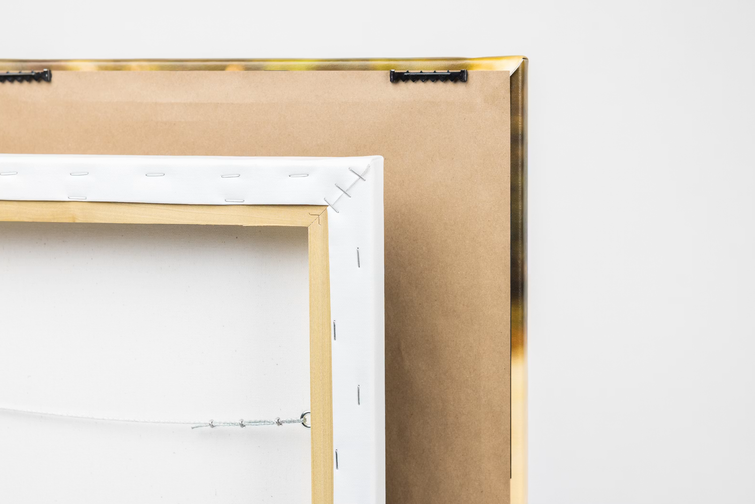 Close-up of a gold picture frame corner showing the back of a canvas stretcher bar on a white background.