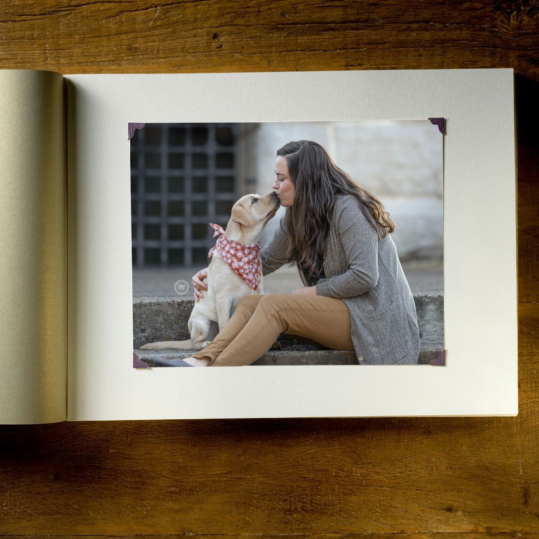 A woman shares a tender moment kissing her yellow Labrador wearing a floral bandana, captured in an open photo album.