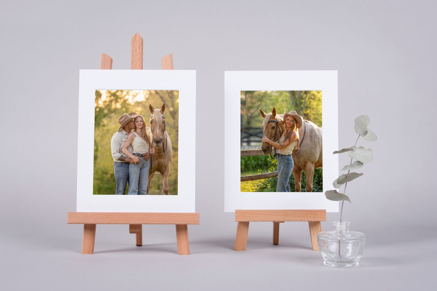 Two framed photos on wooden easels showing a woman with a horse outdoors, displayed beside a small glass vase with eucalyptus.
