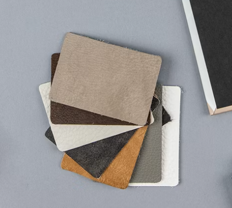Fan of fabric swatches in beige, brown, dark gray, white, and tan leather textures on gray background.