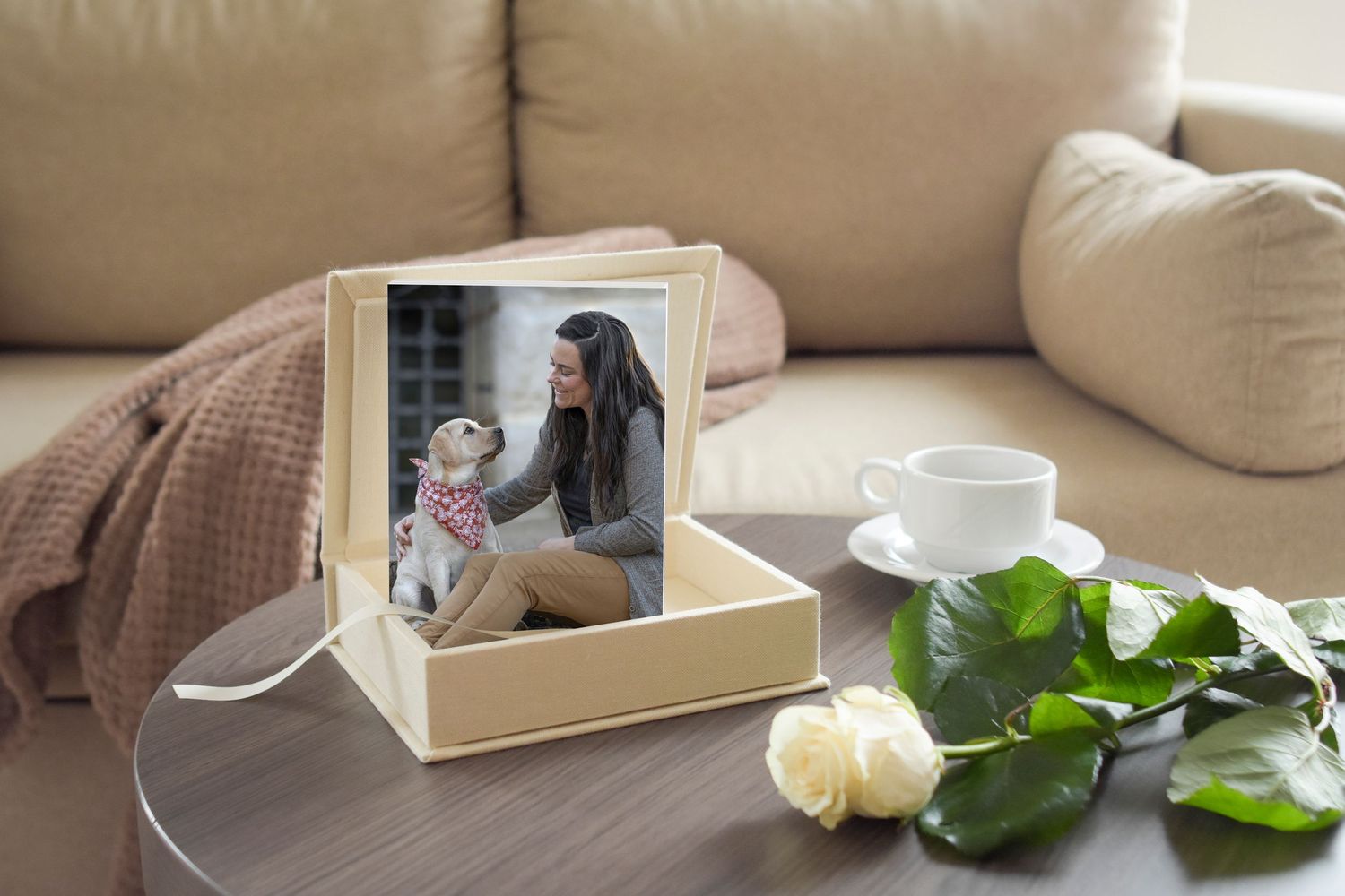 A framed photo of a woman with her dog displayed in a gift box on a coffee table with a white rose.