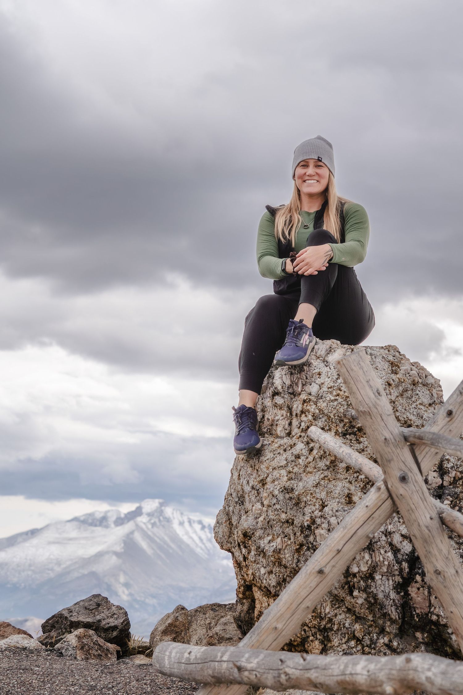 Kait sitting on a rocky outcrop atop Trail Ridge Road in Rocky Mountain National Park under cloudy mountain skies.