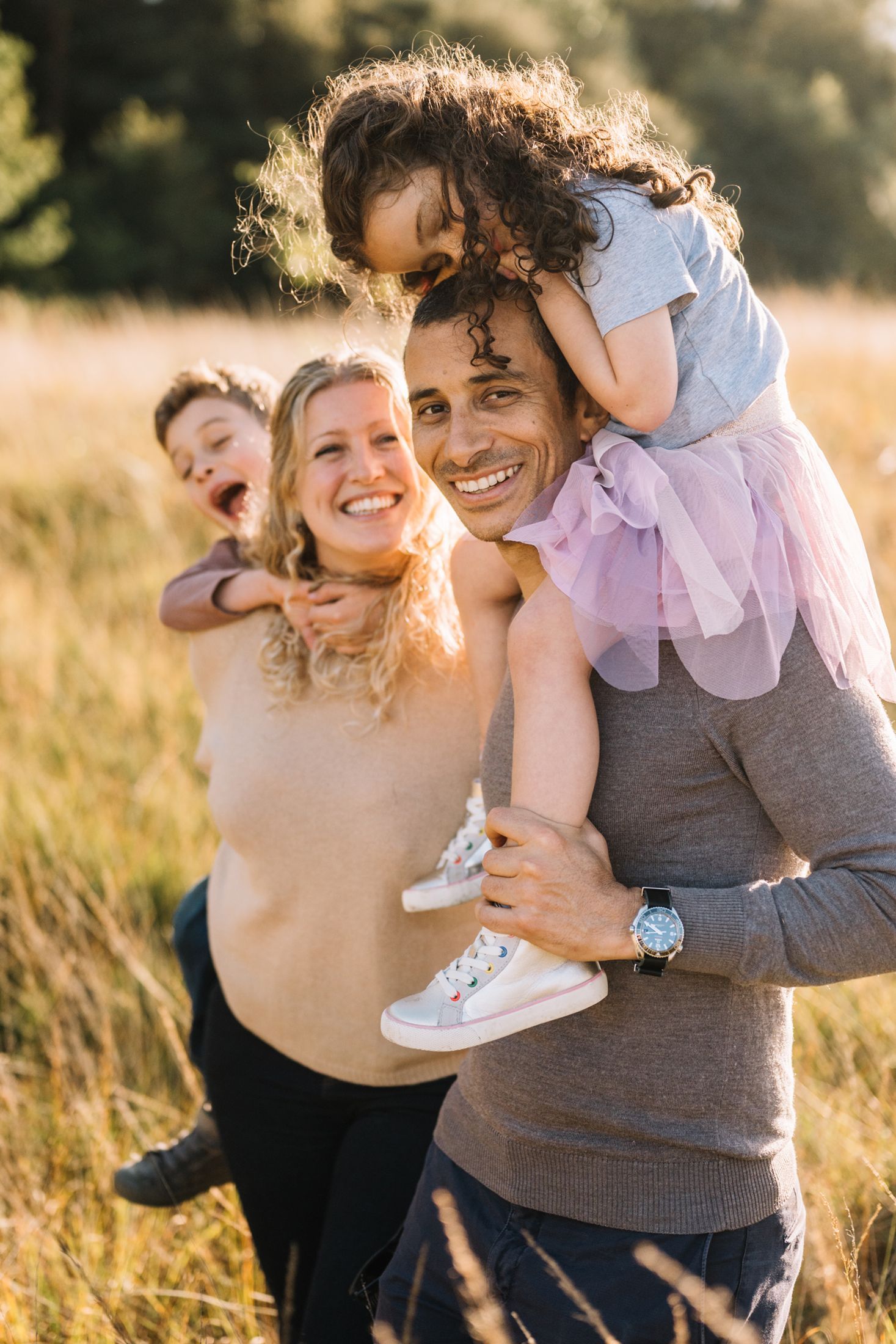 Family enjoying an outdoor photoshoot in a sunlit field, featuring a mother, father, and two children, emphasizing the t
