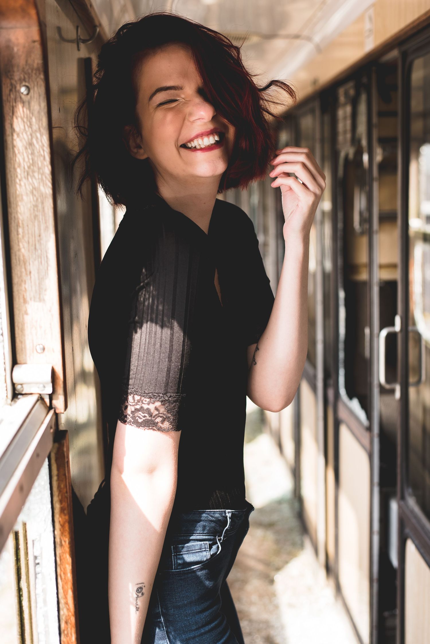 Joyful young woman with short red hair wearing black top laughing in old train car corridor.