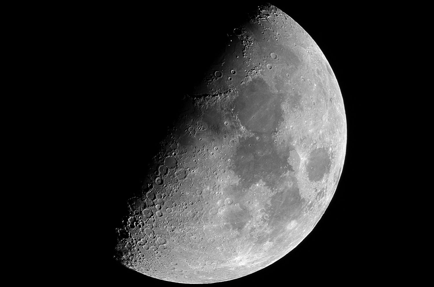 A detailed black and white photograph of a half moon phase showing craters and lunar surface against a dark sky.