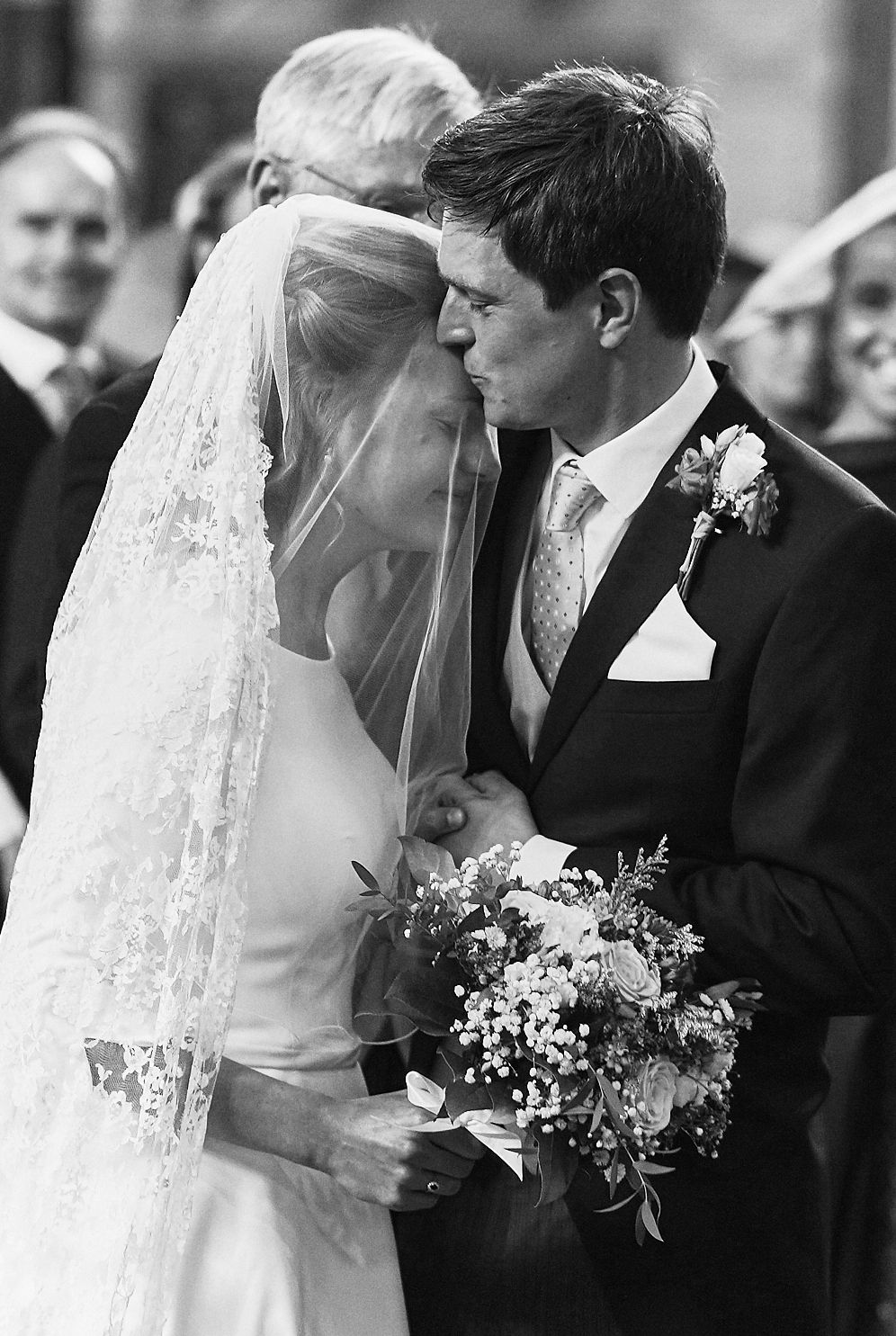 Natural close-up of bride meeting the groom at the altar, kissing on the forehead. Catholic wedding photography Europe.