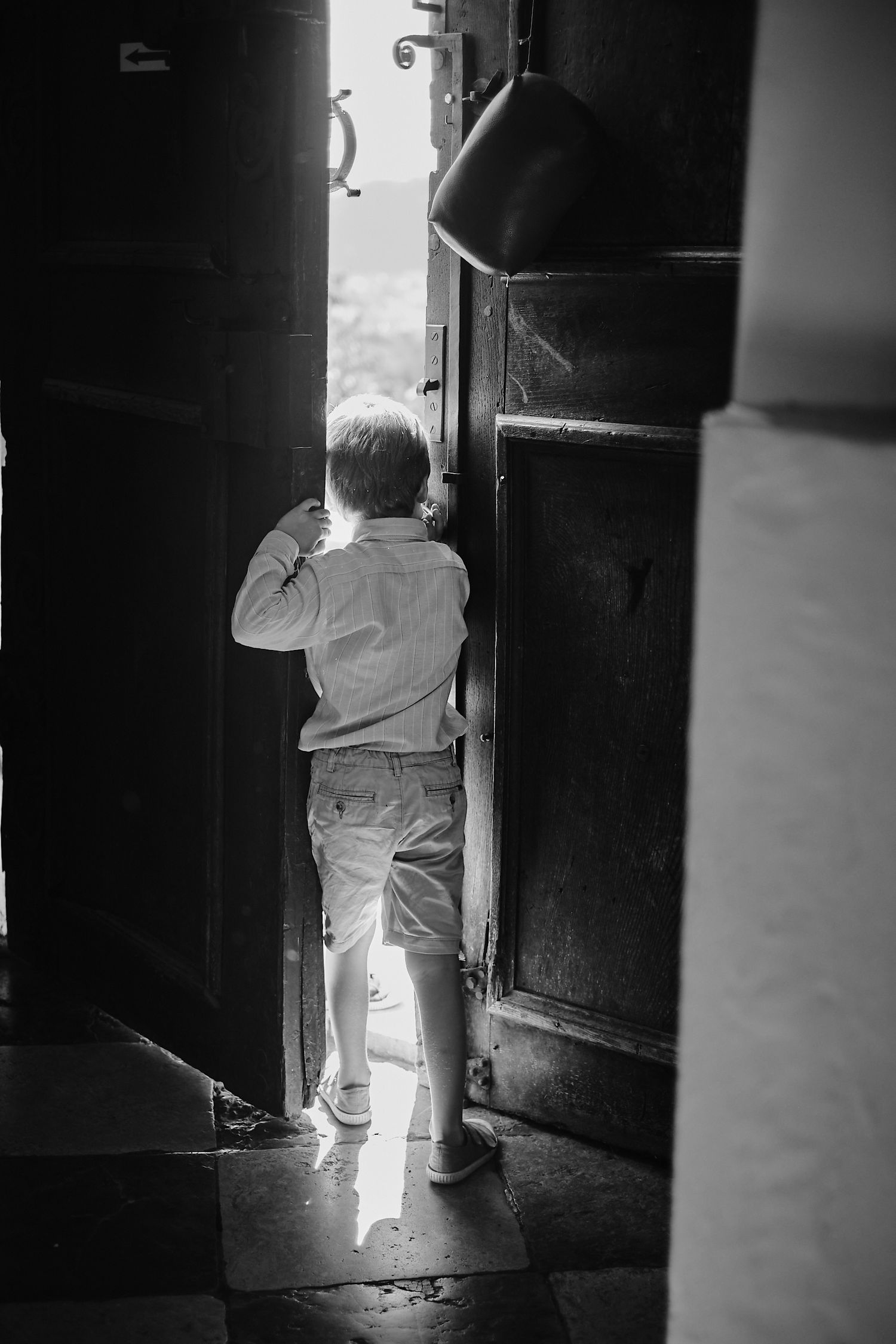 Boy peaking through church door, sunshie entering the room. Dramatic lighting, documentary wedding photography.