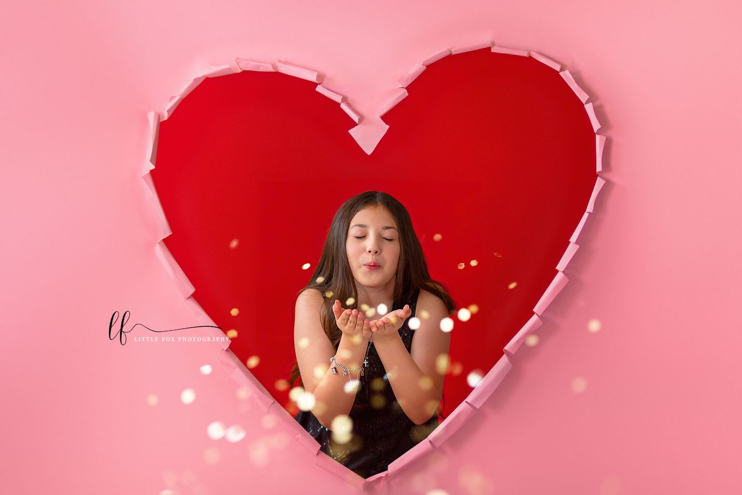 Little girl blowing gold glitter through torn paper heart for portrait