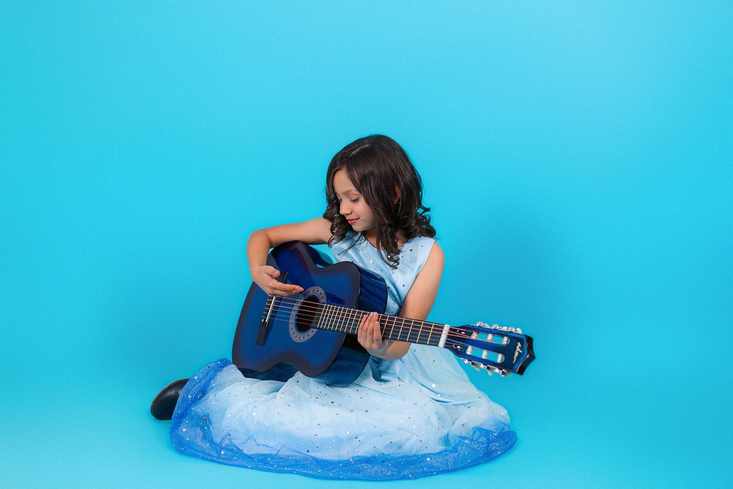 Child musician portrait with blue dress and guitar on blue studio background