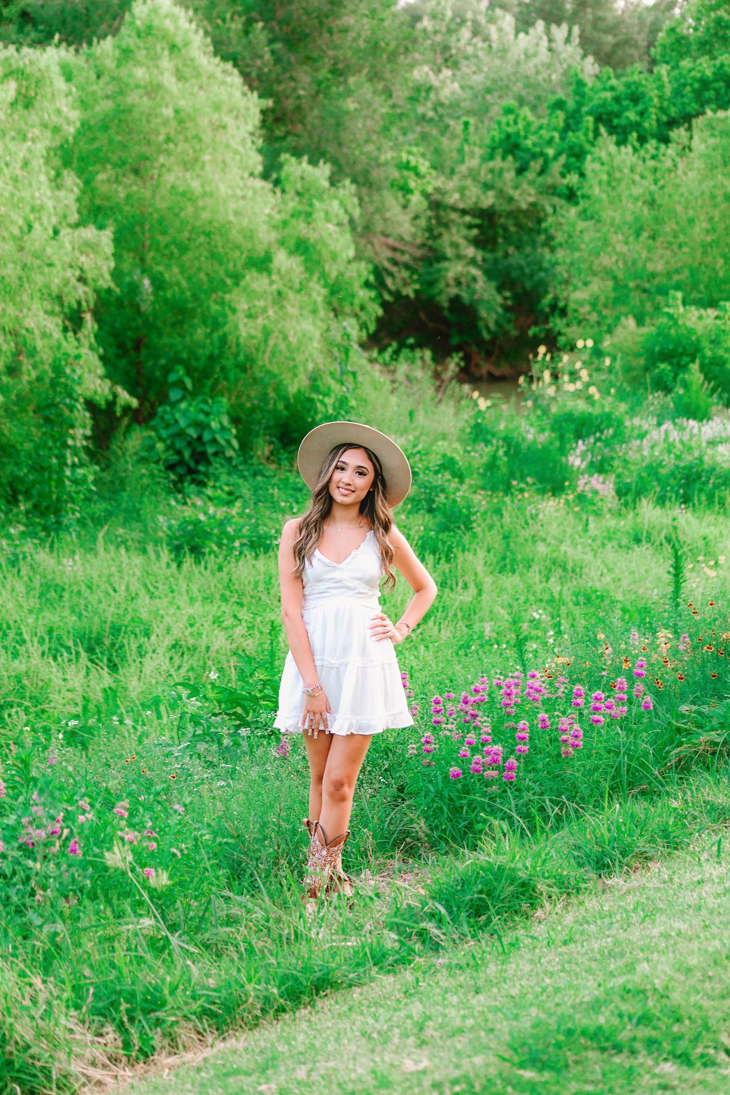 Senior girl in Houston, Texas standing in a field of flowers wearing a sun hat and white dress.