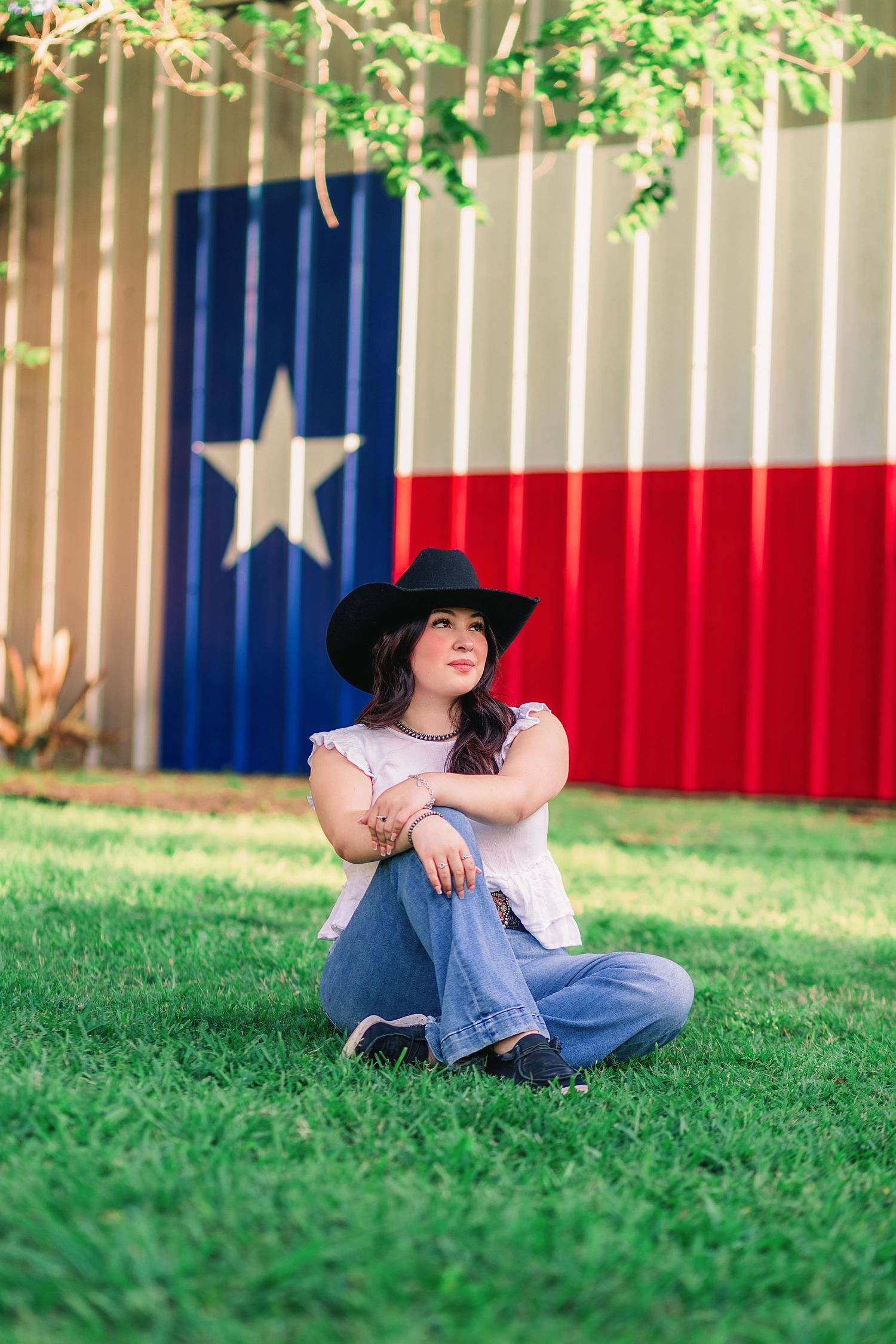 Senior girl in cowgirl attire posing with Texas flag on building behind her