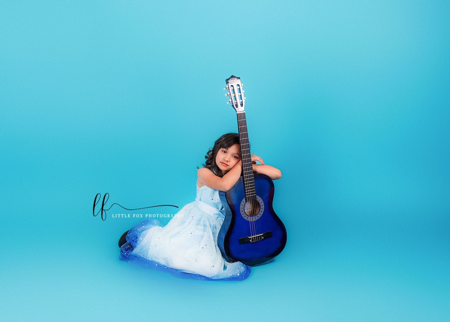 Studio portrait of girl in blue dress with guitar on solid blue backdrop