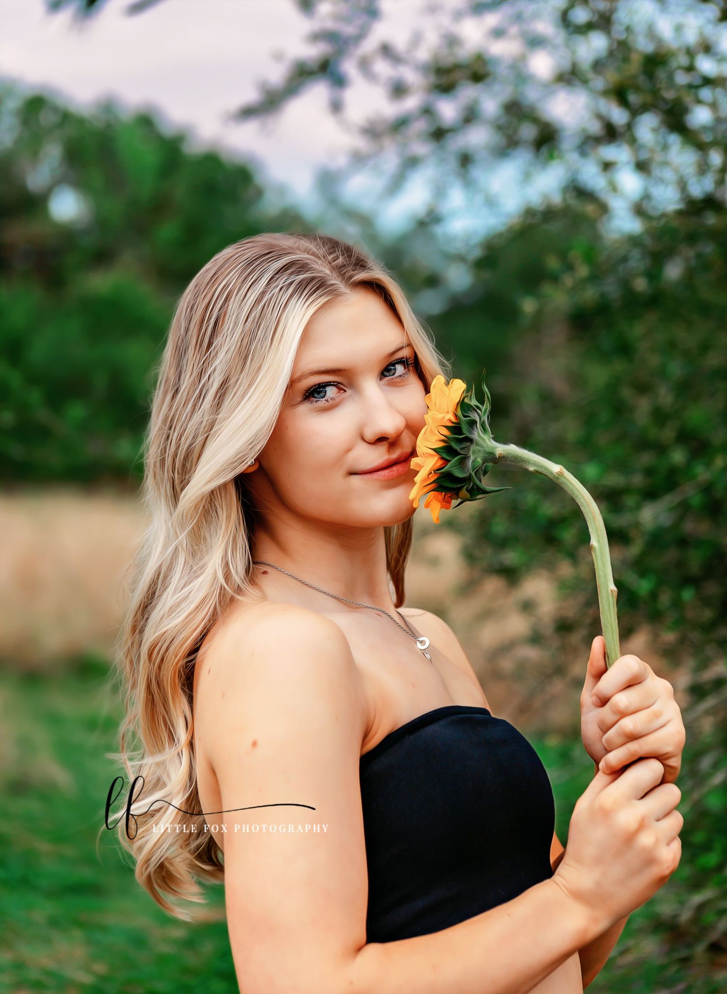 Senior girl gently smelling a large daisy during outdoor portrait session
