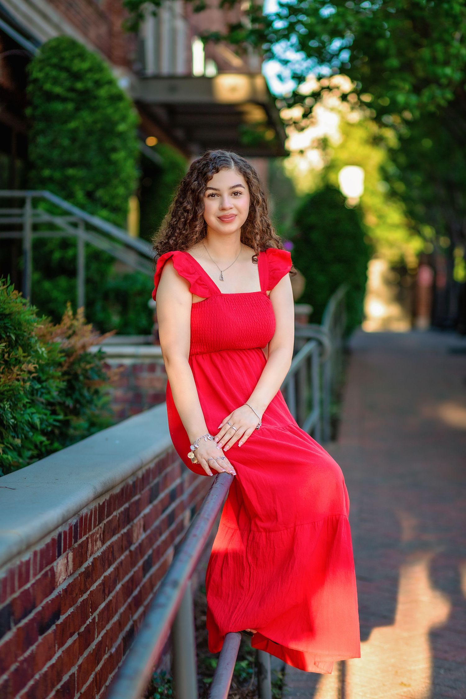Senior girl in red dress sitting on rail during outdoor portrait session