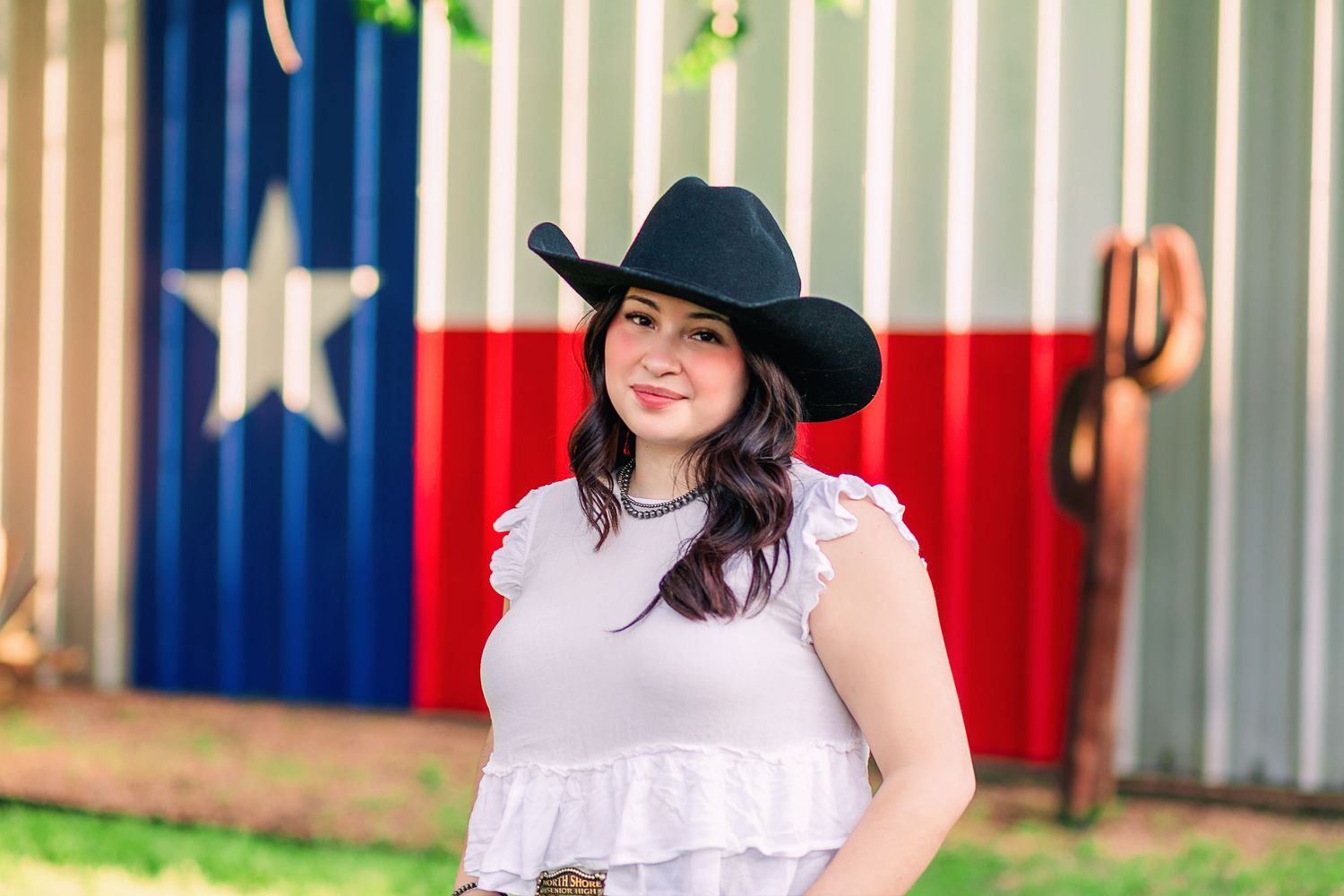 Young woman dressed in cowgirl outfit standing in front of Texas flag mural
