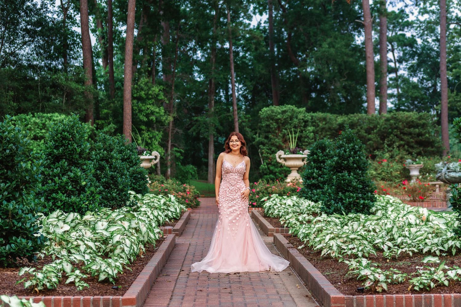 Outdoor prom photo of senior girl in flowing pink dress surrounded by greenery
