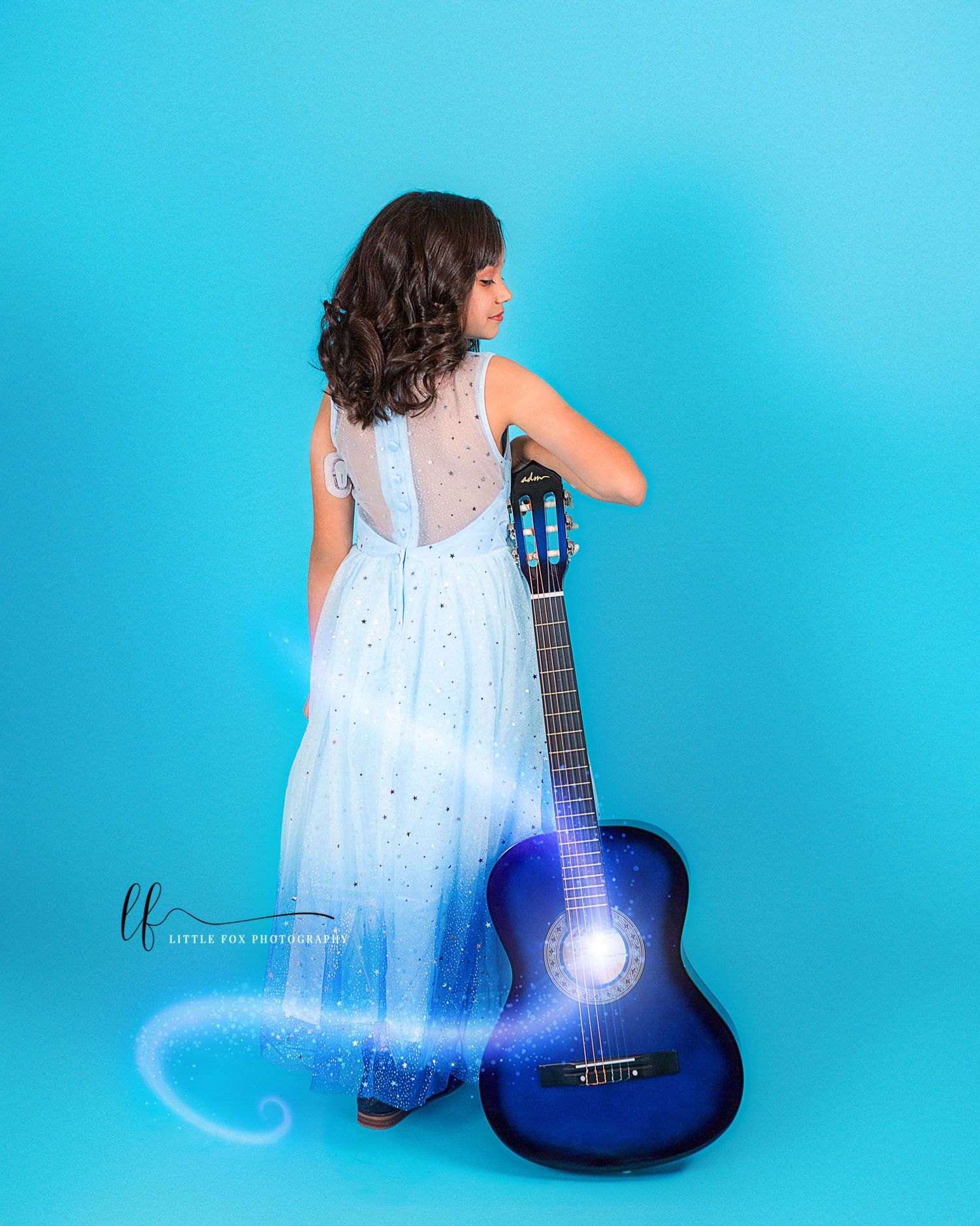 Portrait of little girl in blue dress holding guitar against blue background