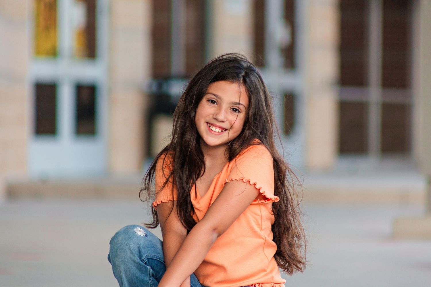 Young girl kneeling in front of school building for portrait photography