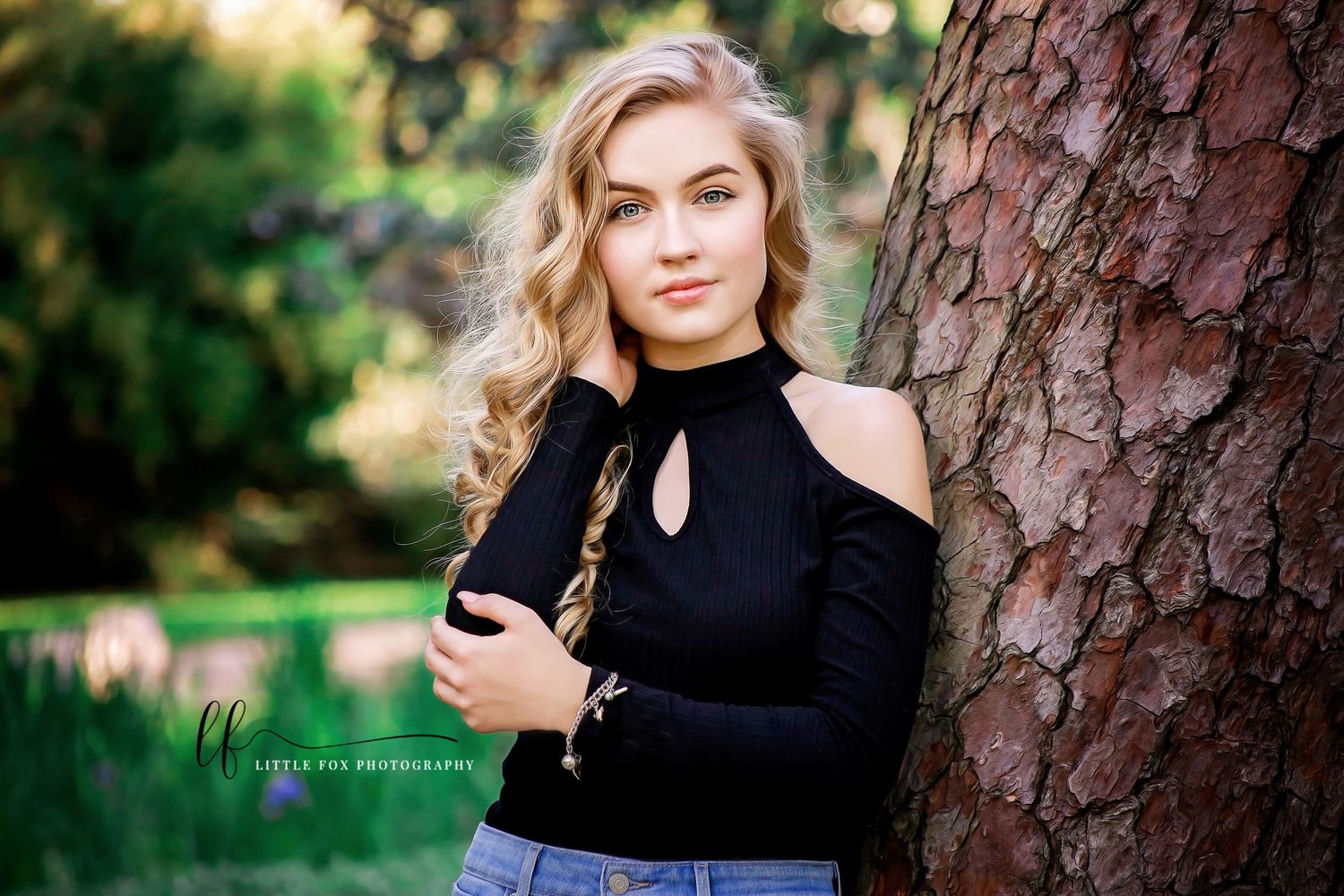 Outdoor senior portrait of girl with golden blonde hair standing near tree