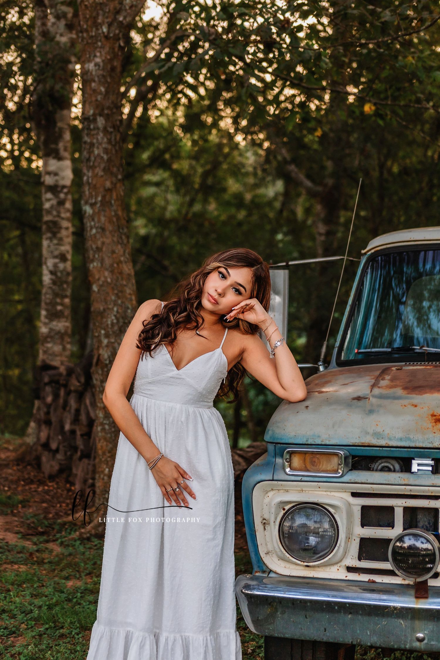 Senior girl leaning on her elbow on the hood of an old blue truck