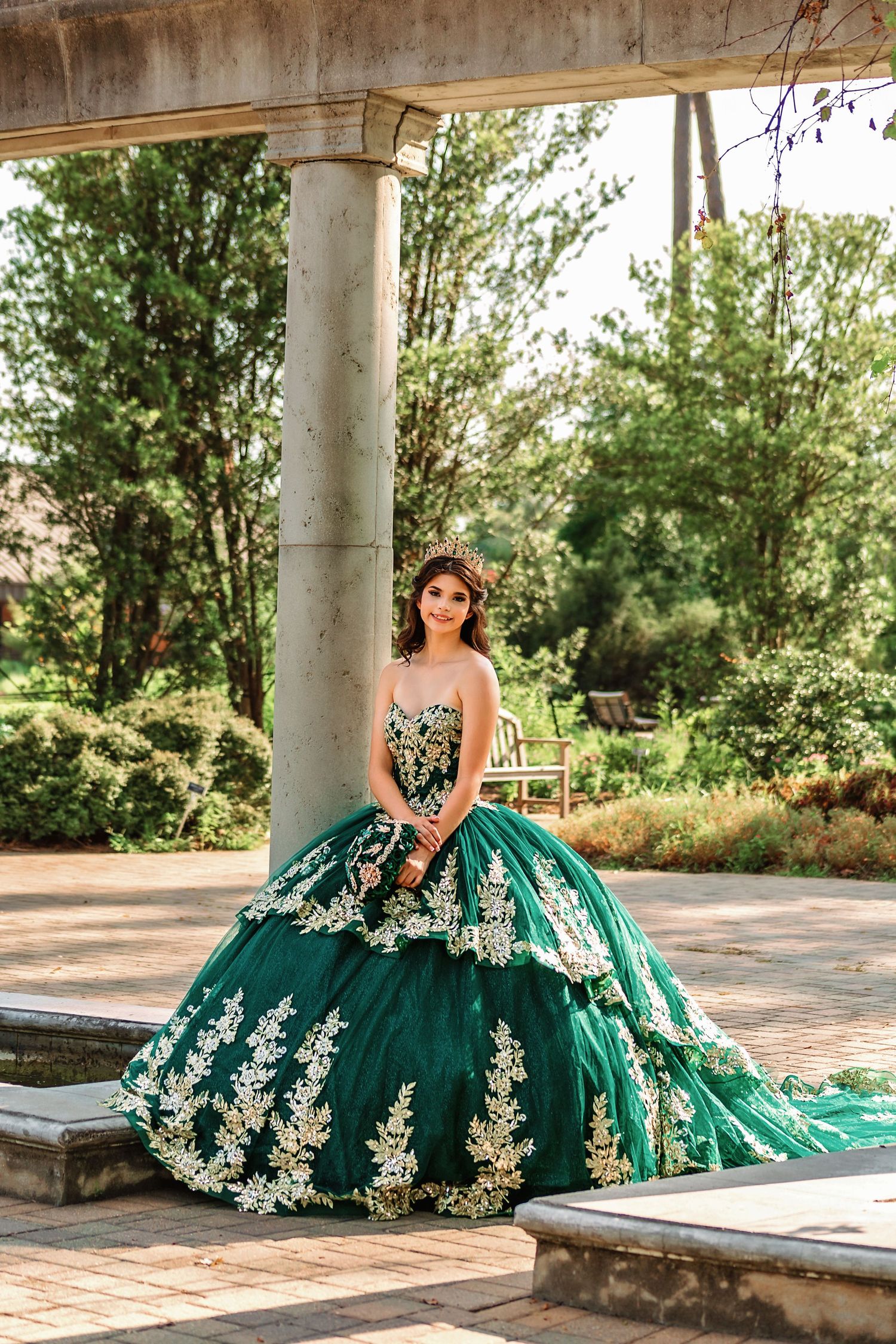 Quinceañera portrait of young girl wearing green and gold dress in park