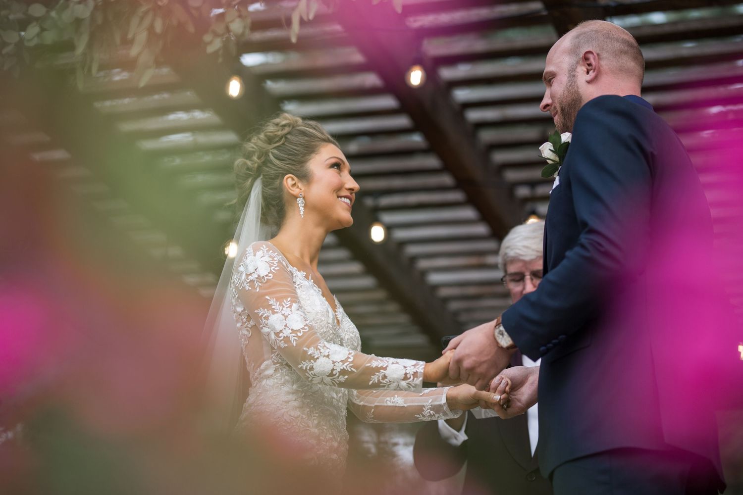 Intimate wedding ceremony moment with pink floral accents in foreground.