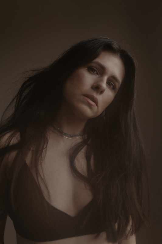 Moody portrait in sepia tones featuring long dark hair and choker necklace against dark background.
